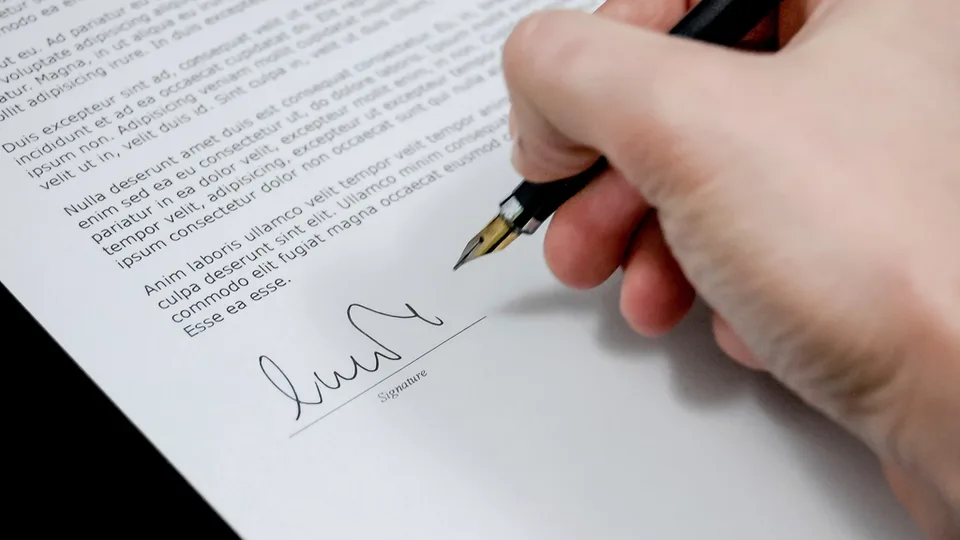 Hands with a pen over a printed contract on a desk