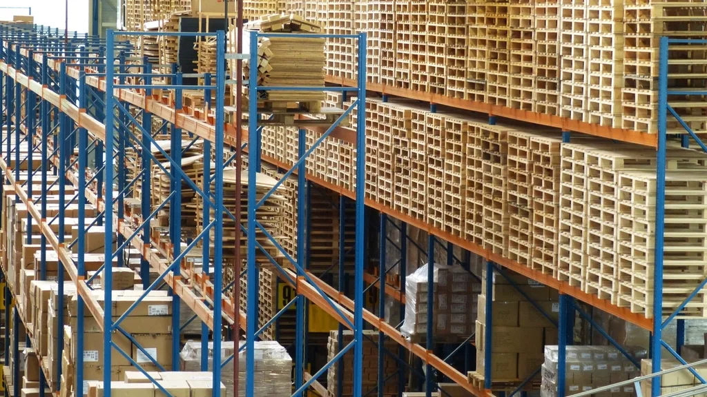 Tall blue warehouse racks stacked with wooden pallets and cartons