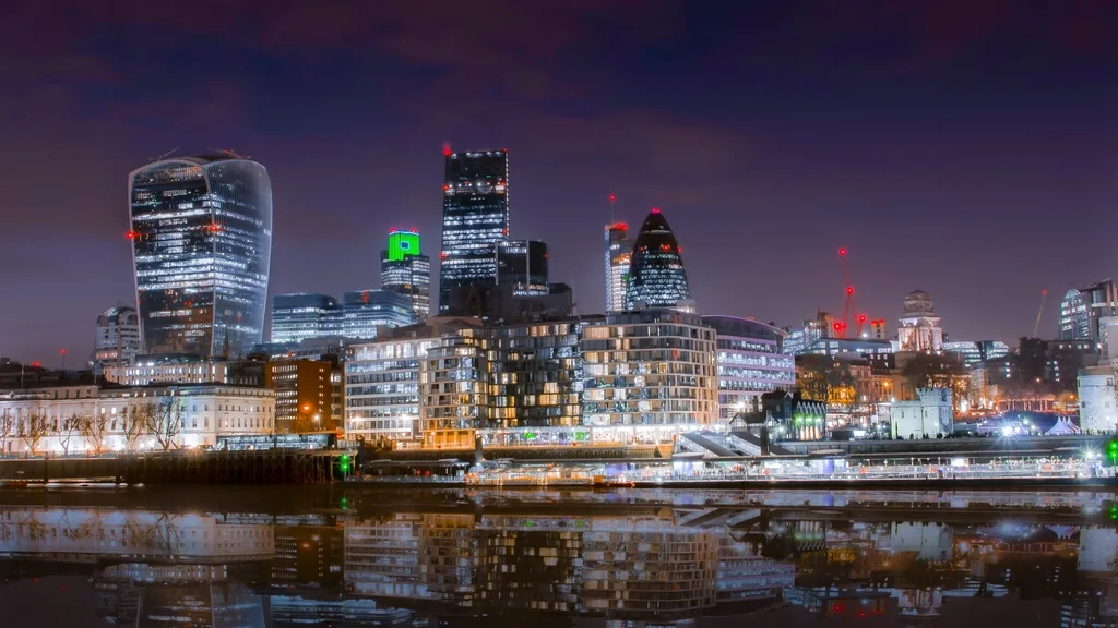 The City of London skyline at night, reflected in the River Thames